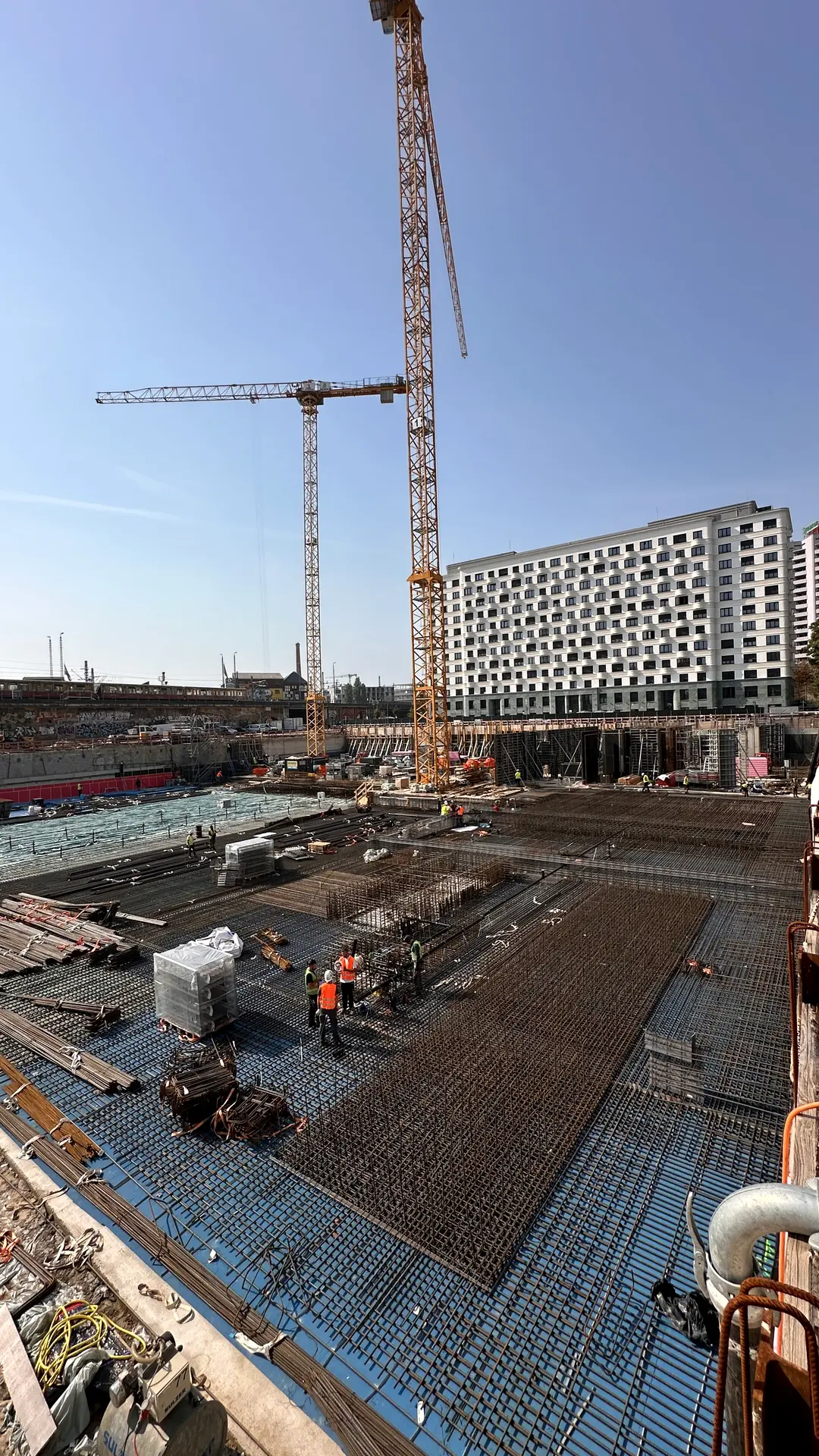 Baustelle mit zwei Kränen und verlegter Bewehrung vor einem Neubau