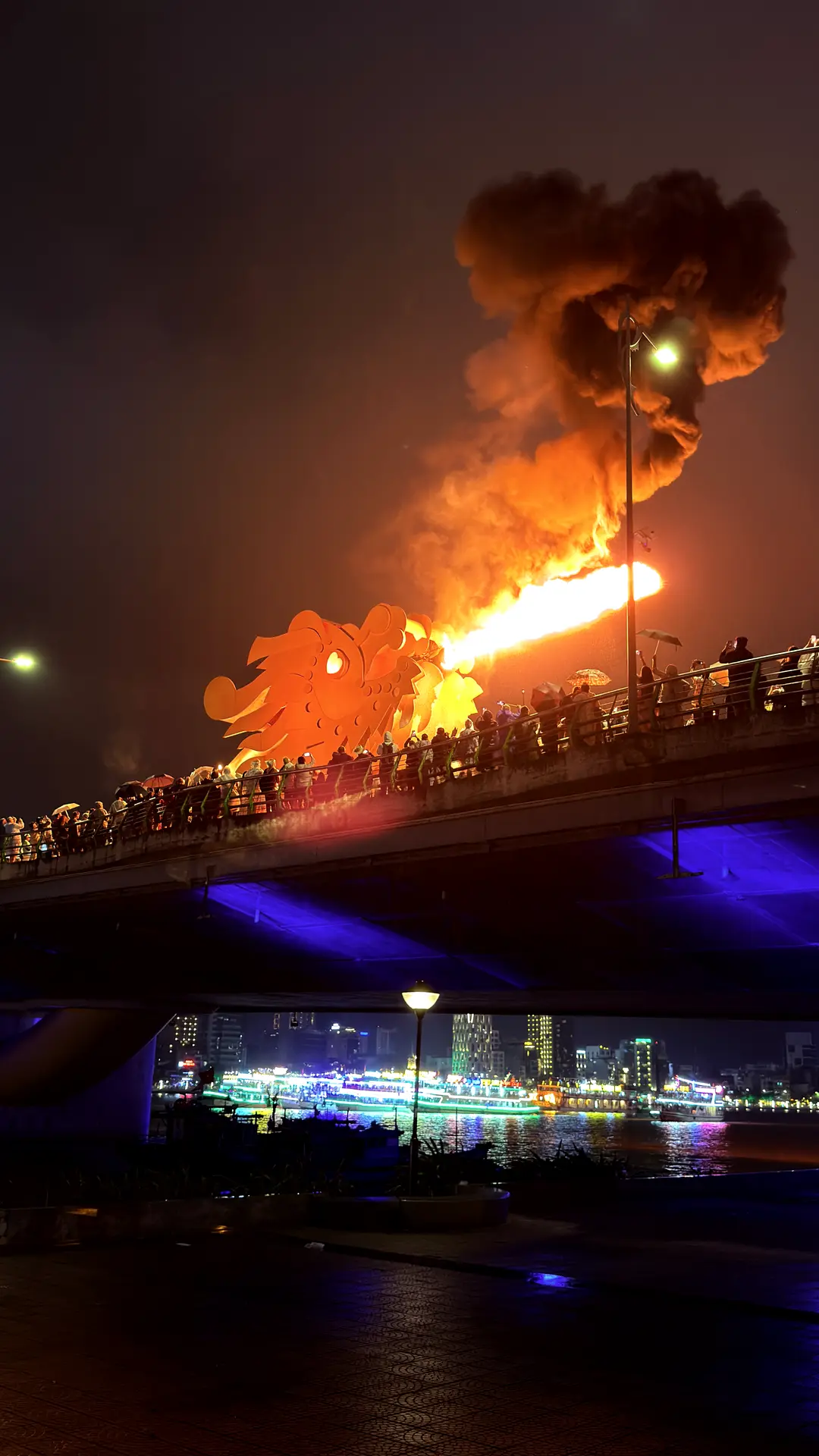 Feuerspeiender Drachenkopf der Drachenbrücke bei Nacht, davor Zuschauer