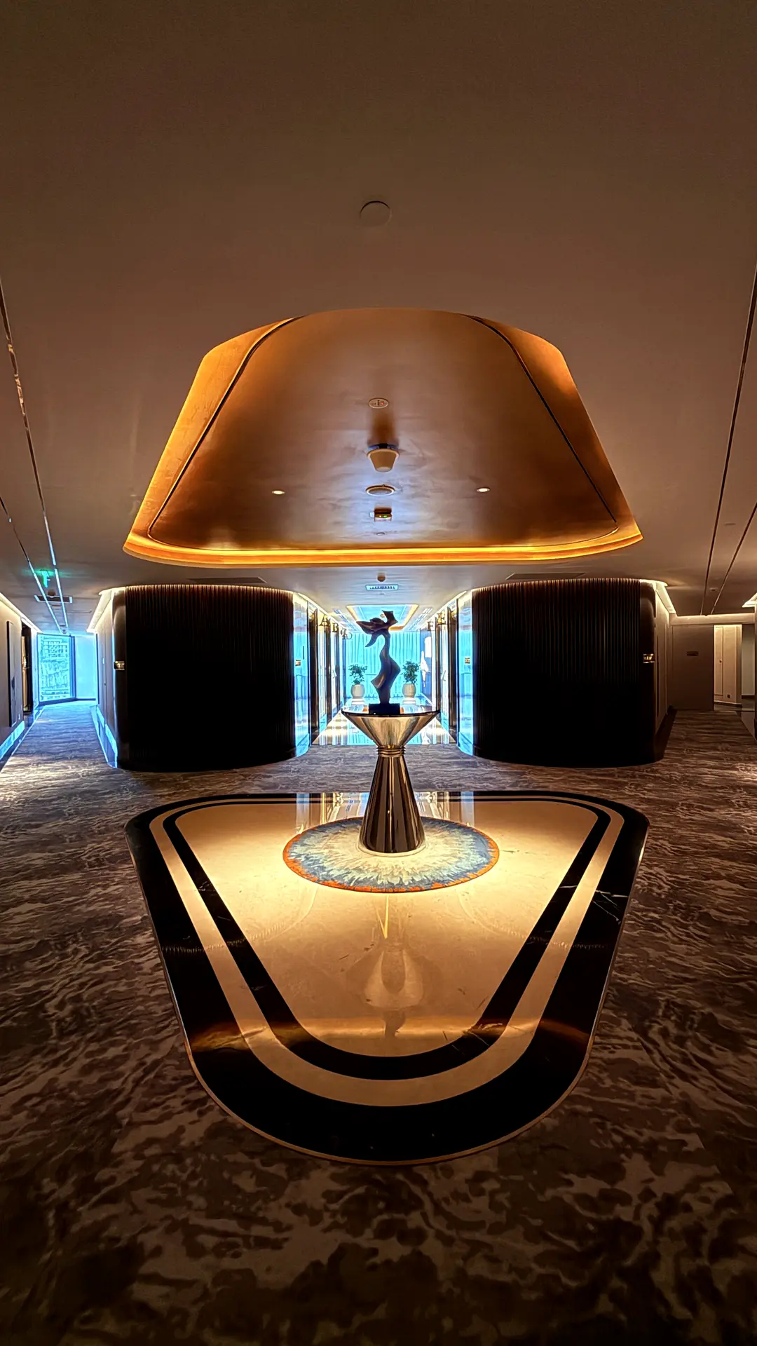 Goldschimmernde Hotellobby mit ovalem Lichtkörper und Intarsienboden