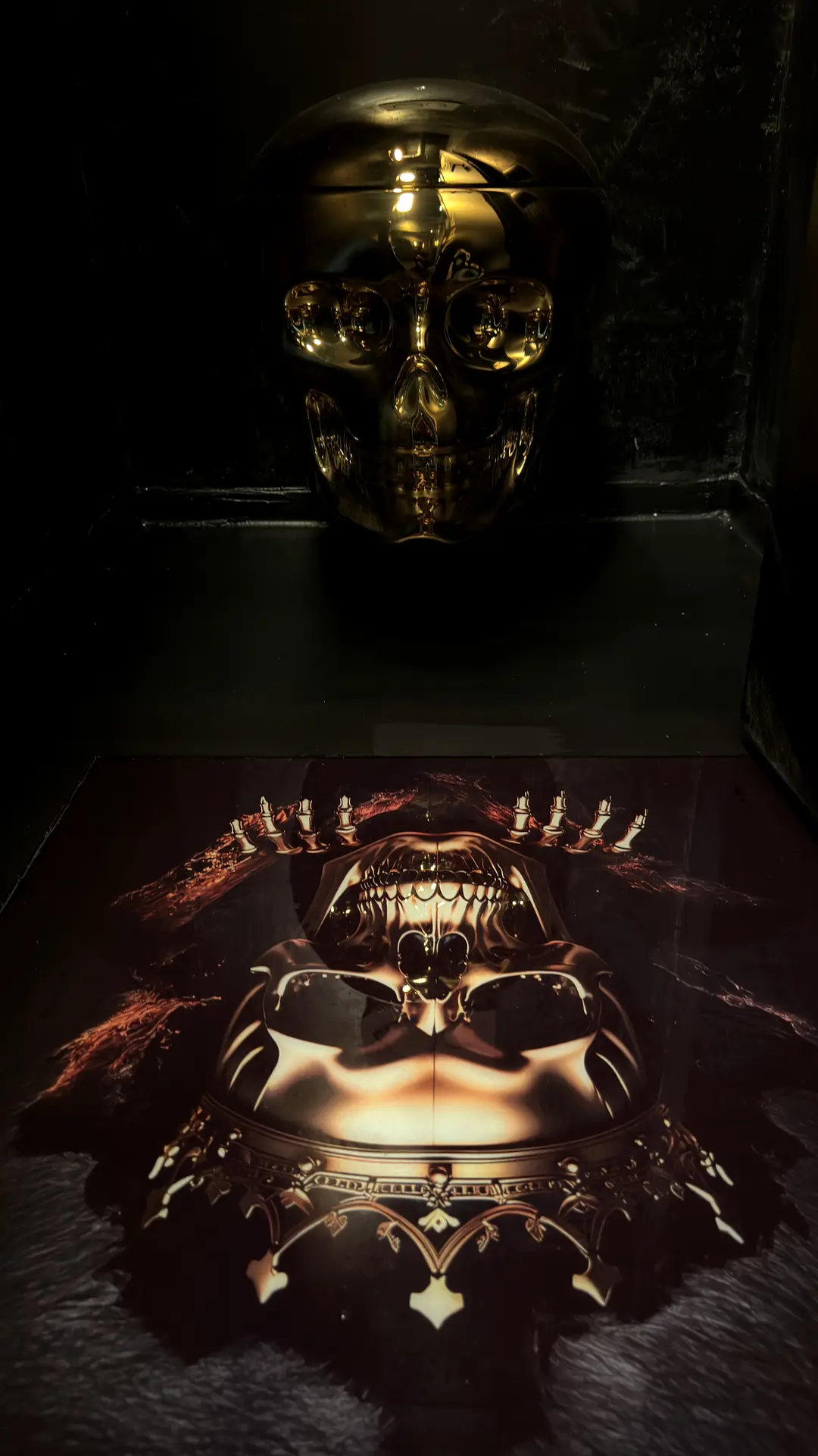 Goldglänzender Totenkopf in einer dunklen Nische über einem gedruckten Schädelmotiv