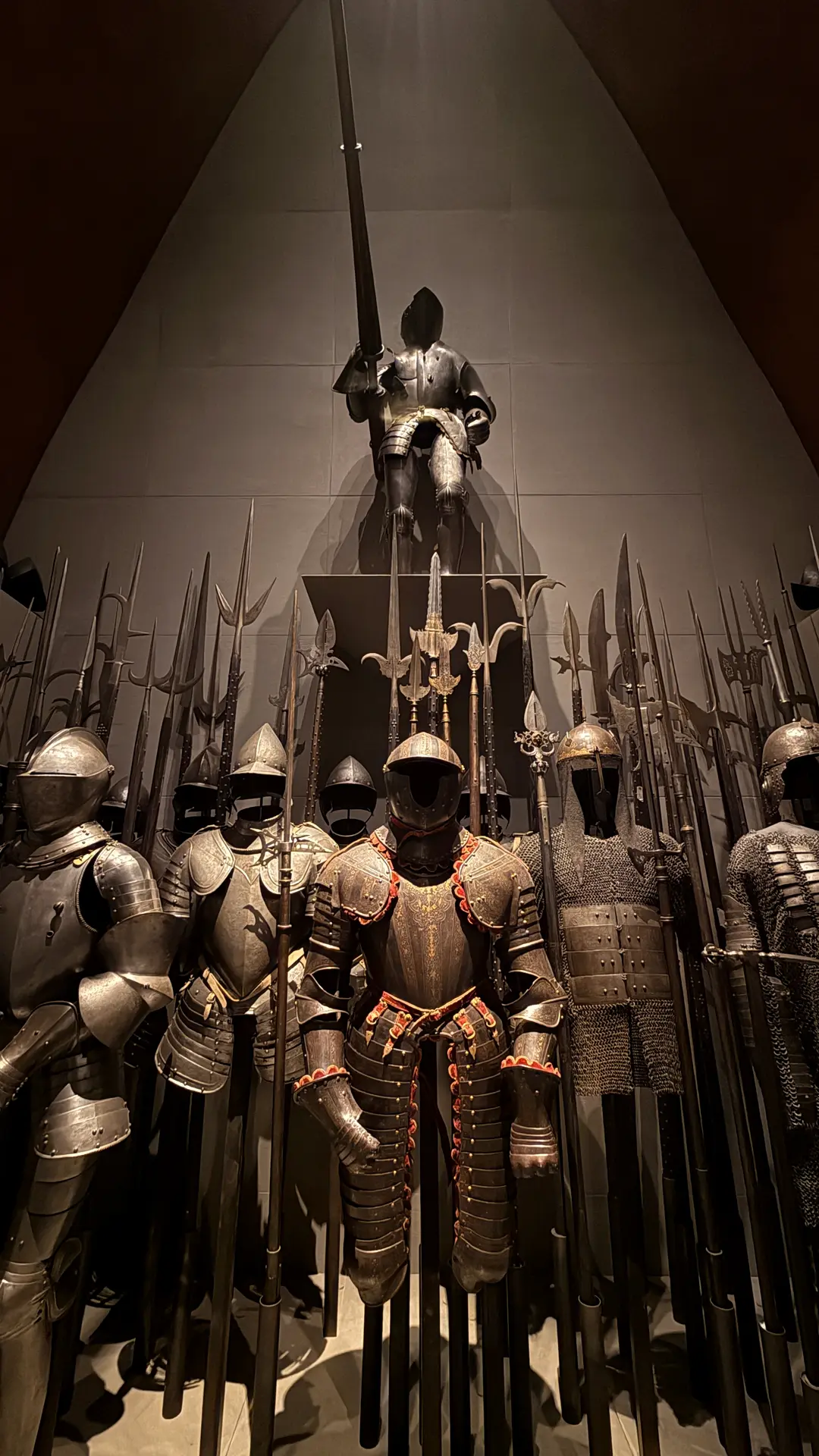 Historische Ritterrüstungen und Stangenwaffen dicht gestaffelt im Museumslicht
