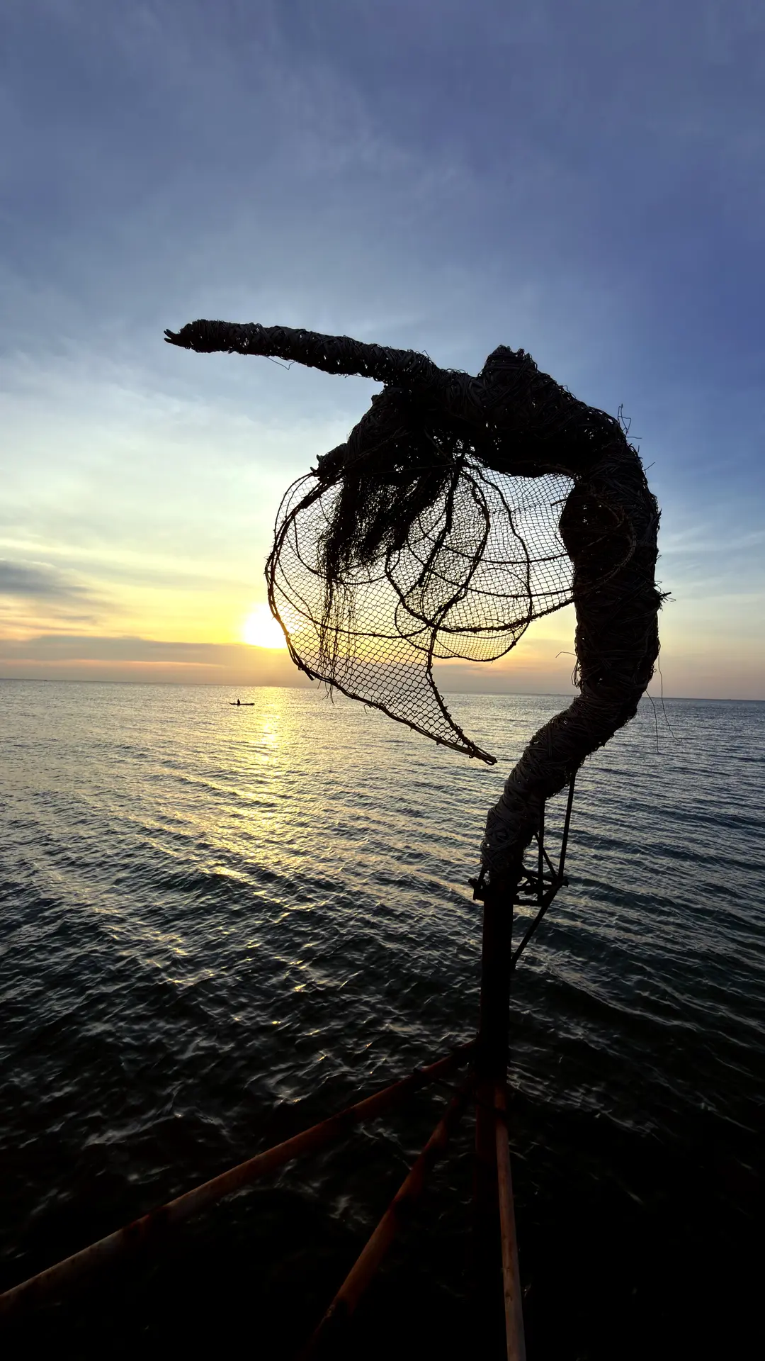 Filigrane Drahtskulptur einer geflügelten Tänzerin vor dem Sonnenuntergang über dem Meer
