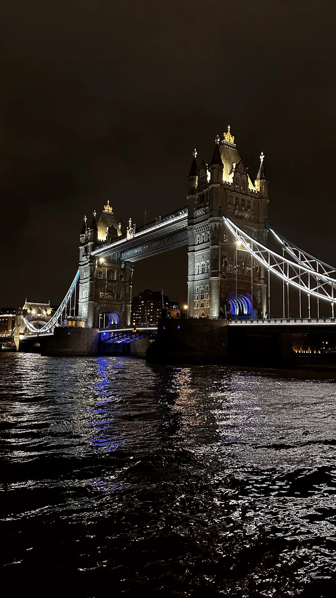 Beleuchtete Tower Bridge bei Nacht über dunklem, bewegtem Wasser