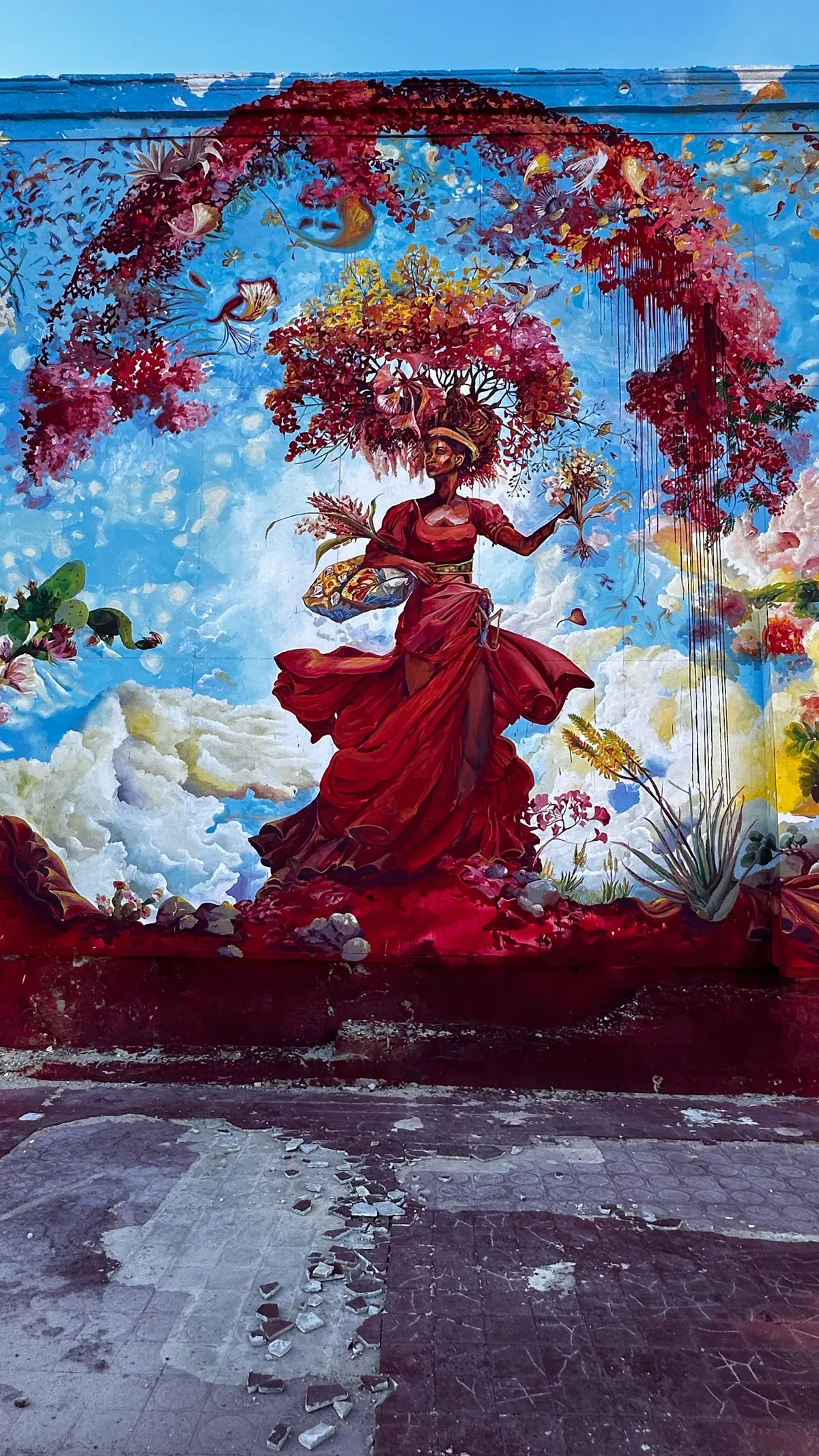 Large mural of a woman in a red dress with a tree of flowers for hair on a weathered wall