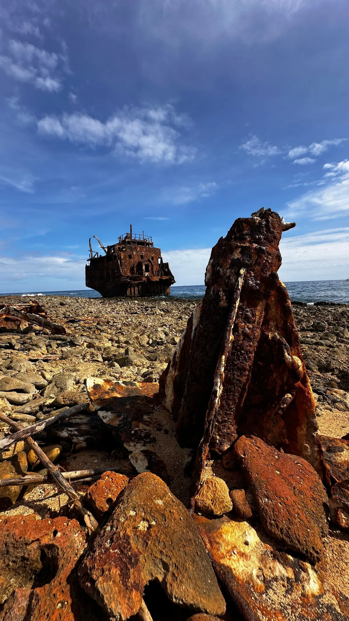 Rusting shipwreck on a rocky shore of Klein Curaçao, a crooked rusty pole in the foreground
