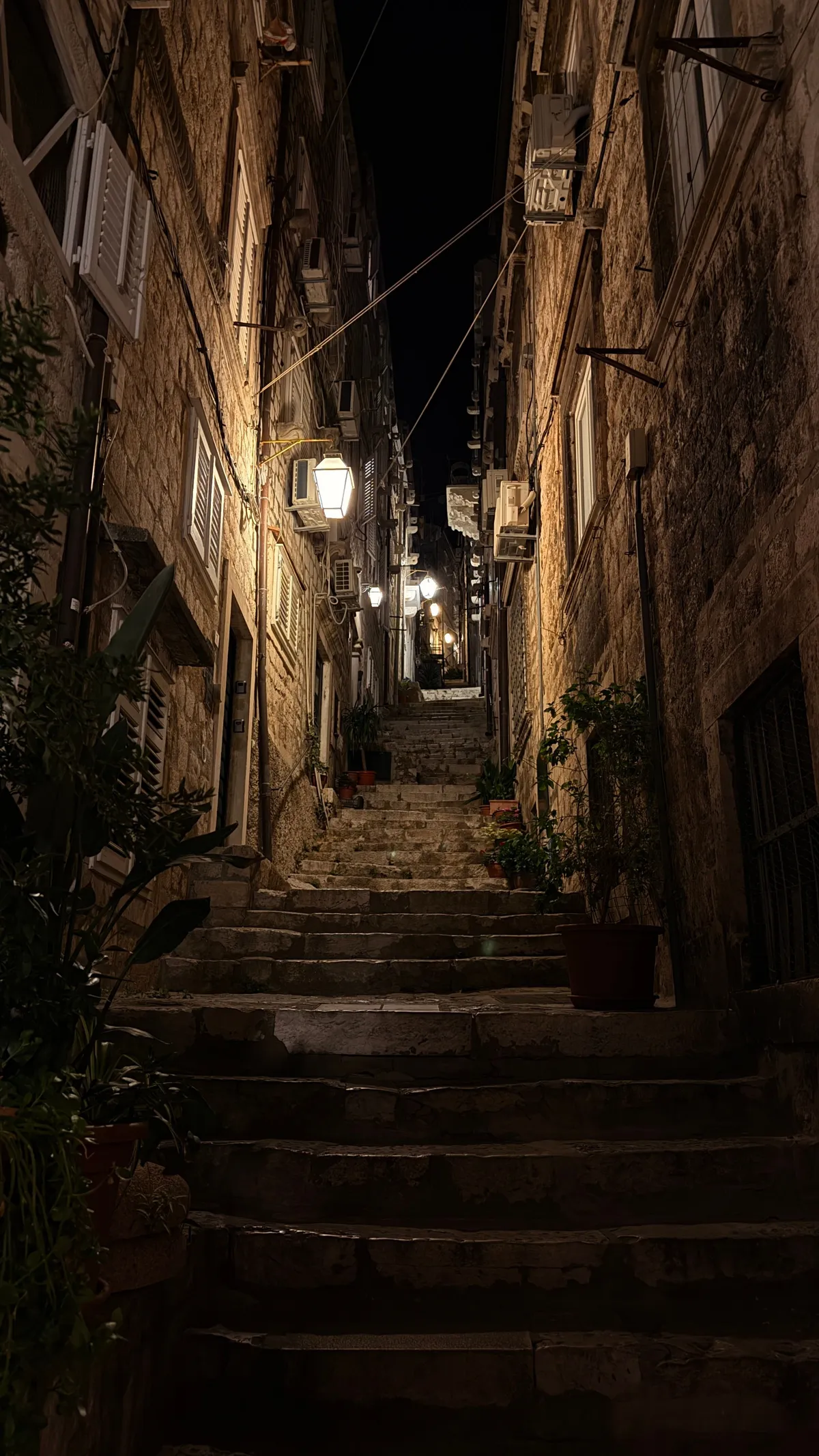 Steep old-town alley in Dubrovnik with stairs and lanterns at night