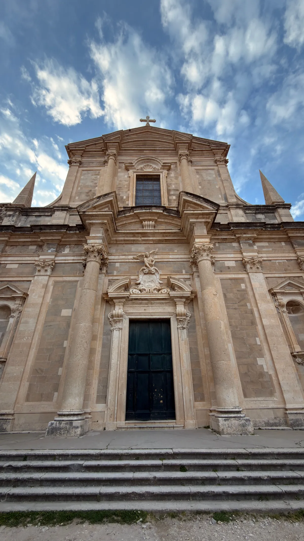 Baroque facade of the Jesuit church in Dubrovnik, centred low-angle view, clouds streaking above