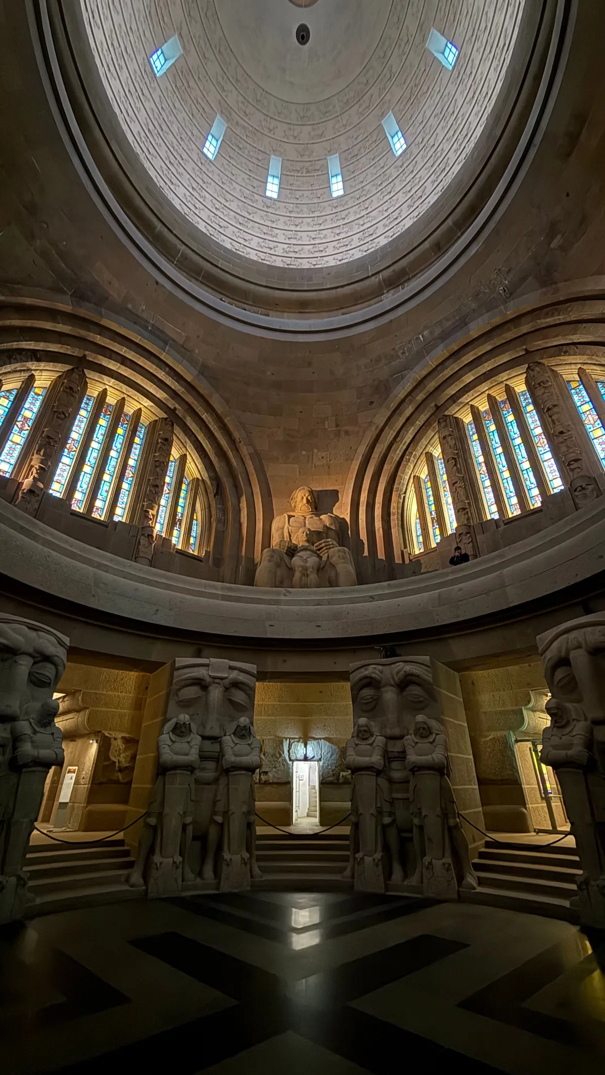 Domed hall of the Monument to the Battle of the Nations with stone guardian figures and rings of light
