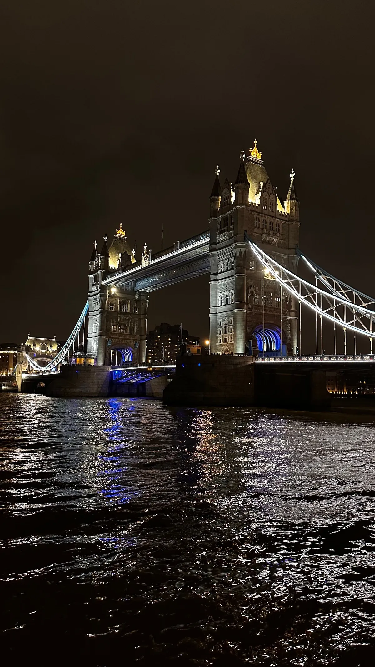 Illuminated Tower Bridge at night above dark, moving water