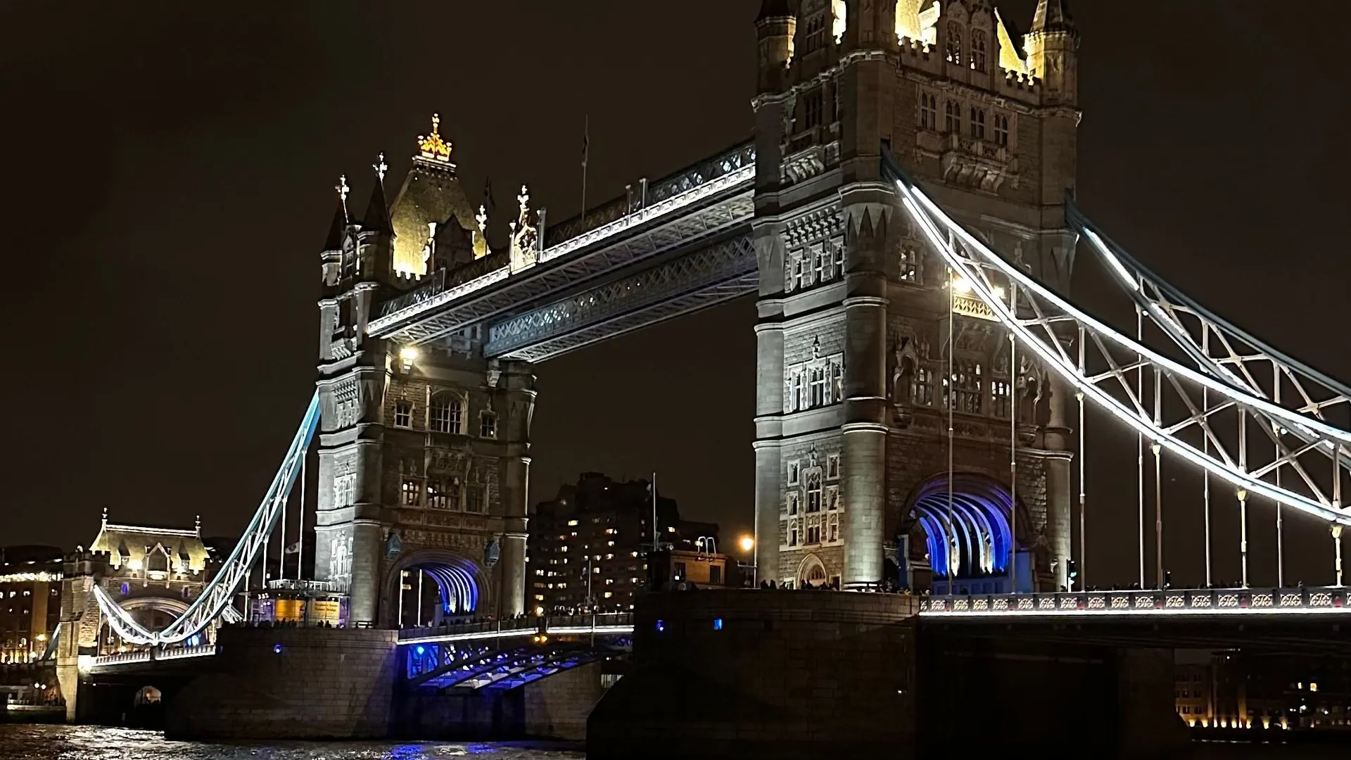 Illuminated Tower Bridge at night above dark, moving water