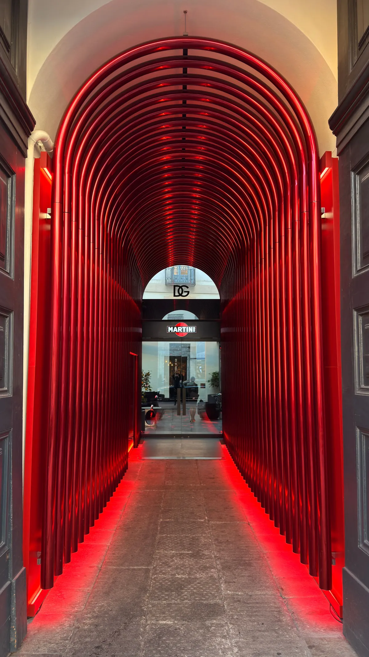 Walk-through installation of glowing red arches forming a tunnel towards a bright doorway