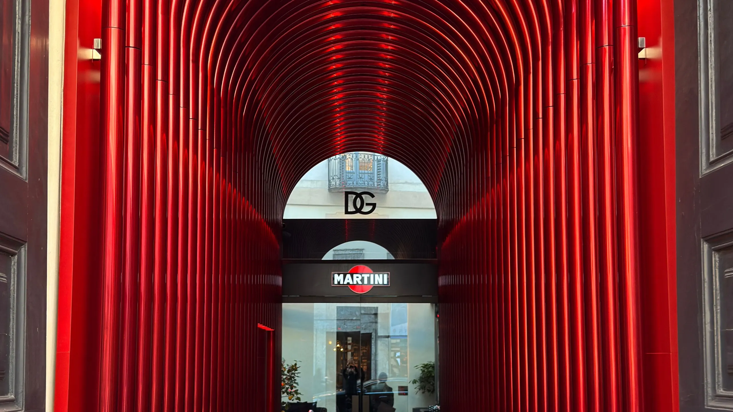 Walk-through installation of glowing red arches forming a tunnel towards a bright doorway