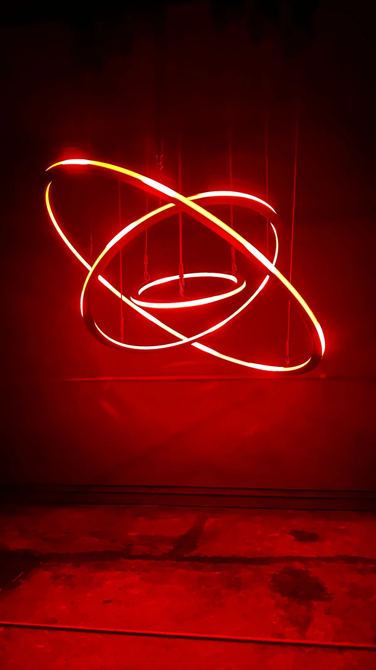 Three glowing red neon rings intersecting in a dark room