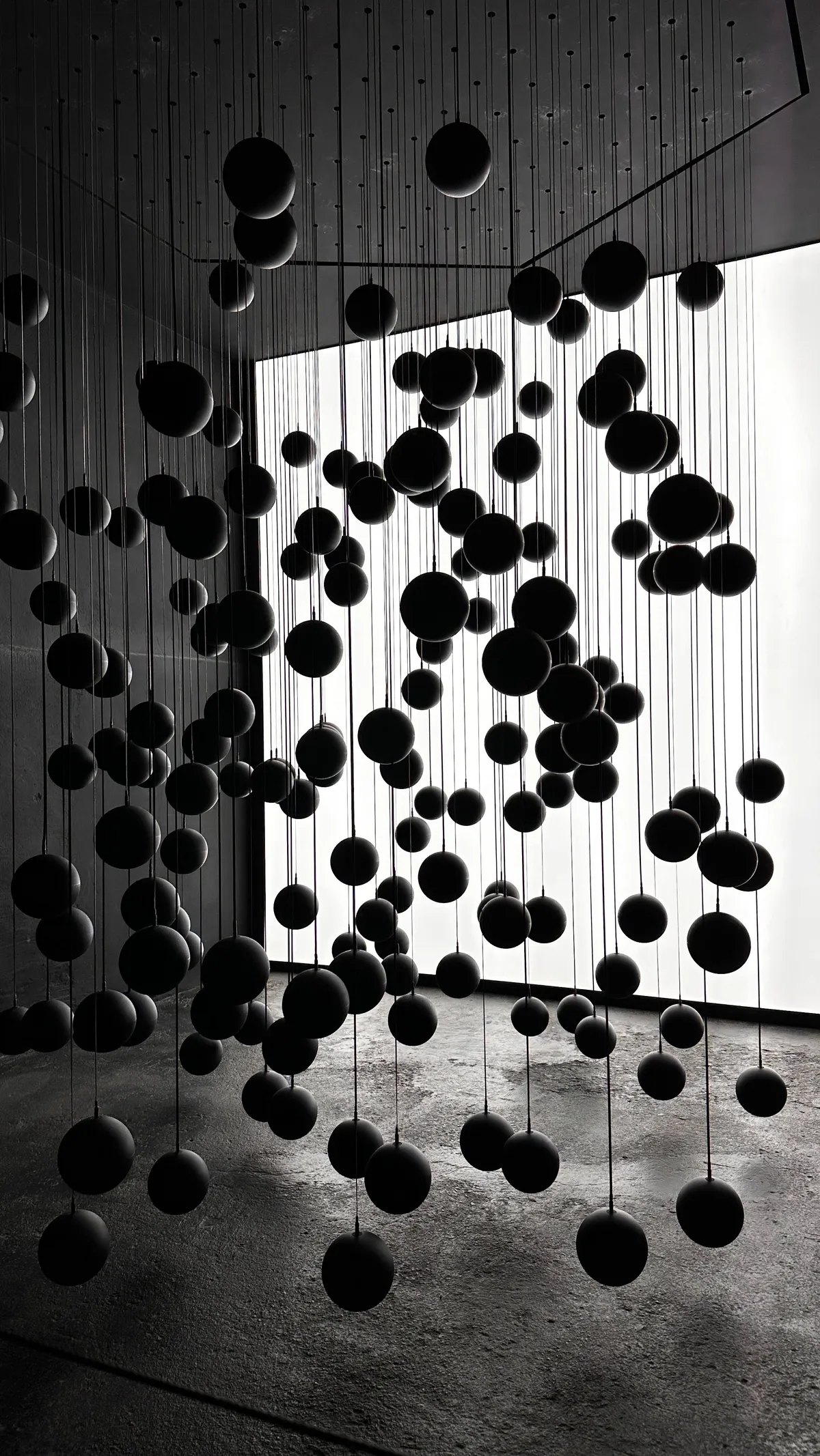 Black spheres suspended on wires in a bright white room, black and white