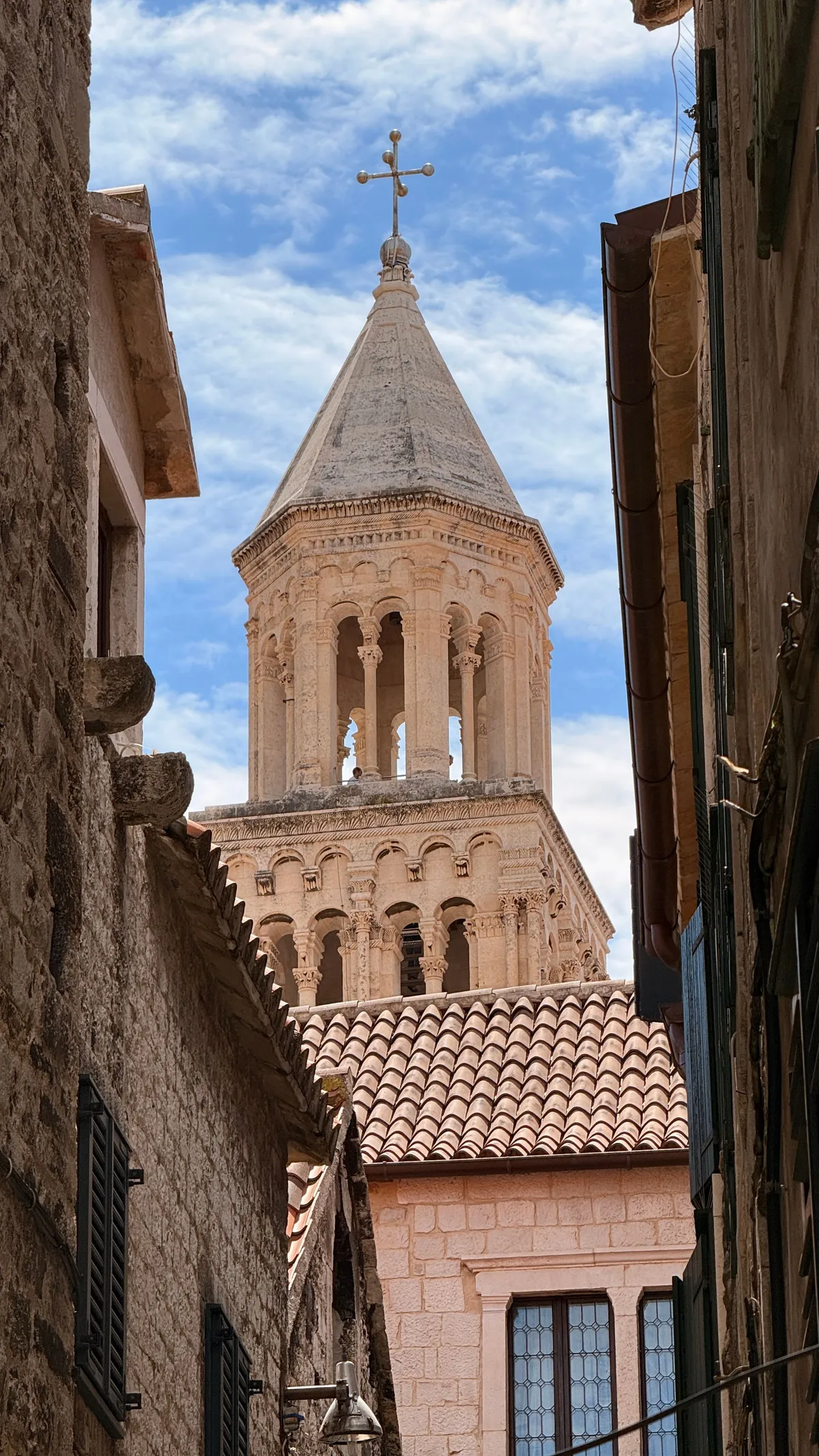 Bell tower of Split cathedral seen from a narrow alley of the palace, sky between the walls