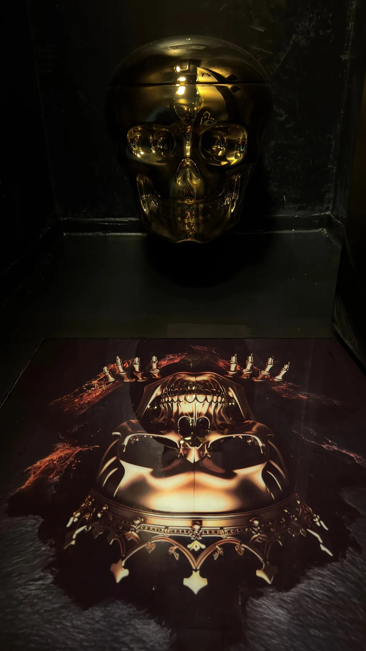 Gold-gleaming skull in a dark niche above a printed skull artwork