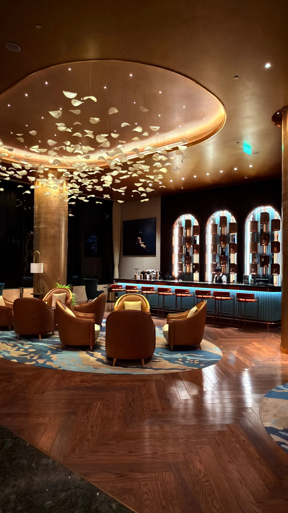 Hotel bar with a ceiling of illuminated butterfly-shaped lights, leather armchairs and a back-lit bottle wall
