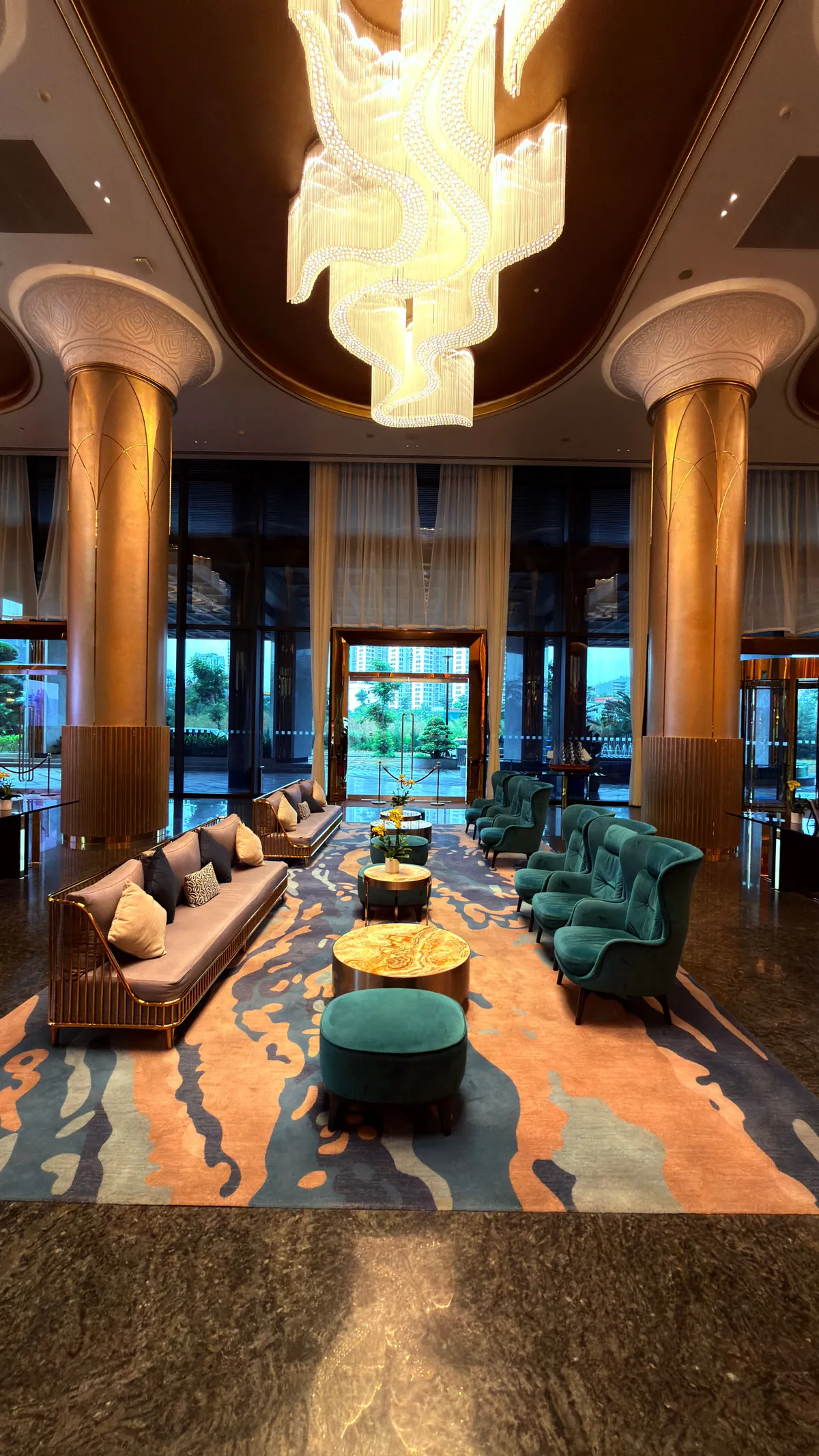 Cascading crystal chandelier between two stone columns above teal and copper lounge chairs in a hotel lobby
