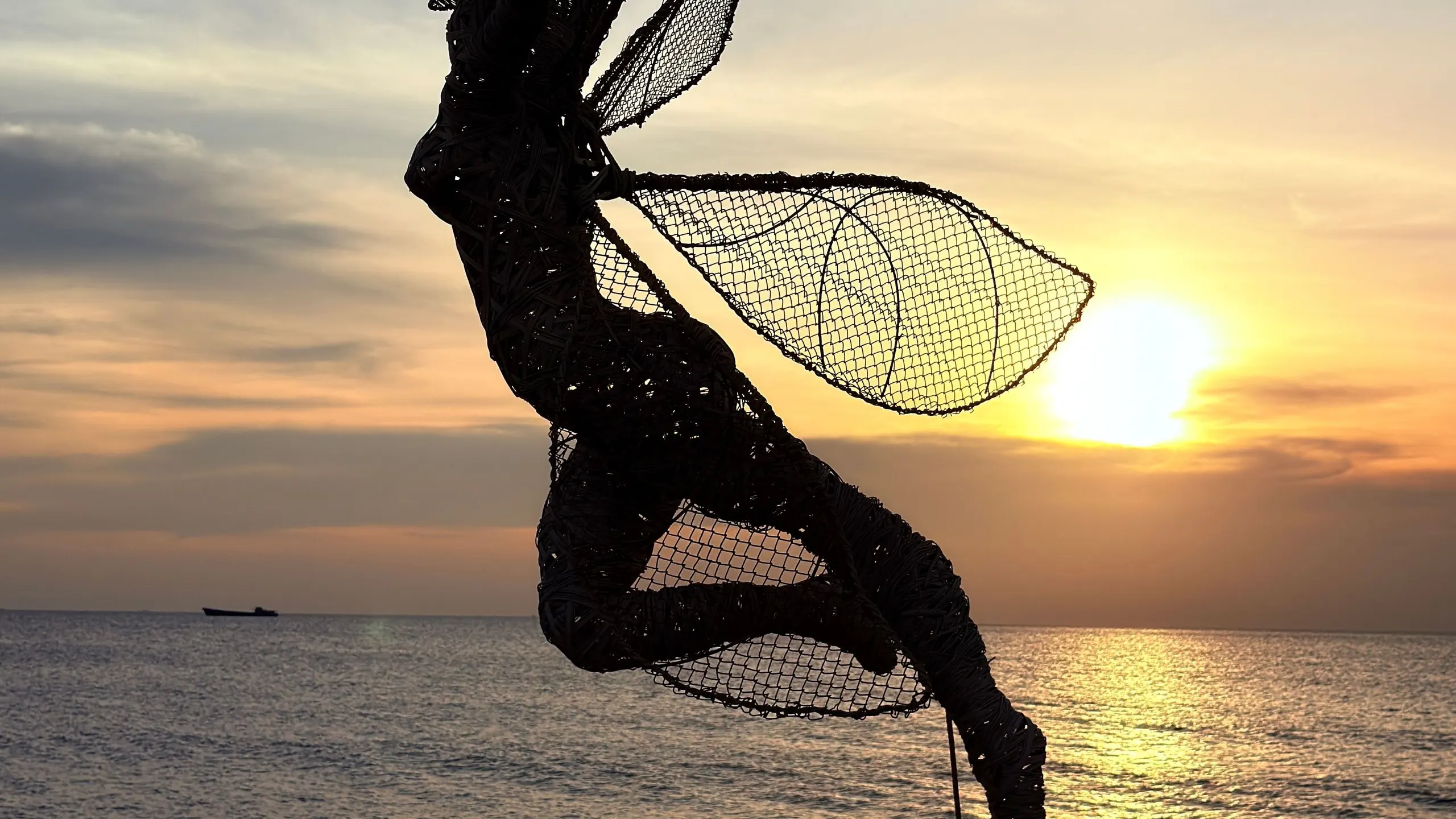 Wire sculpture of a fairy on a pole in silhouette against an orange sunset over the sea at Phu Quoc