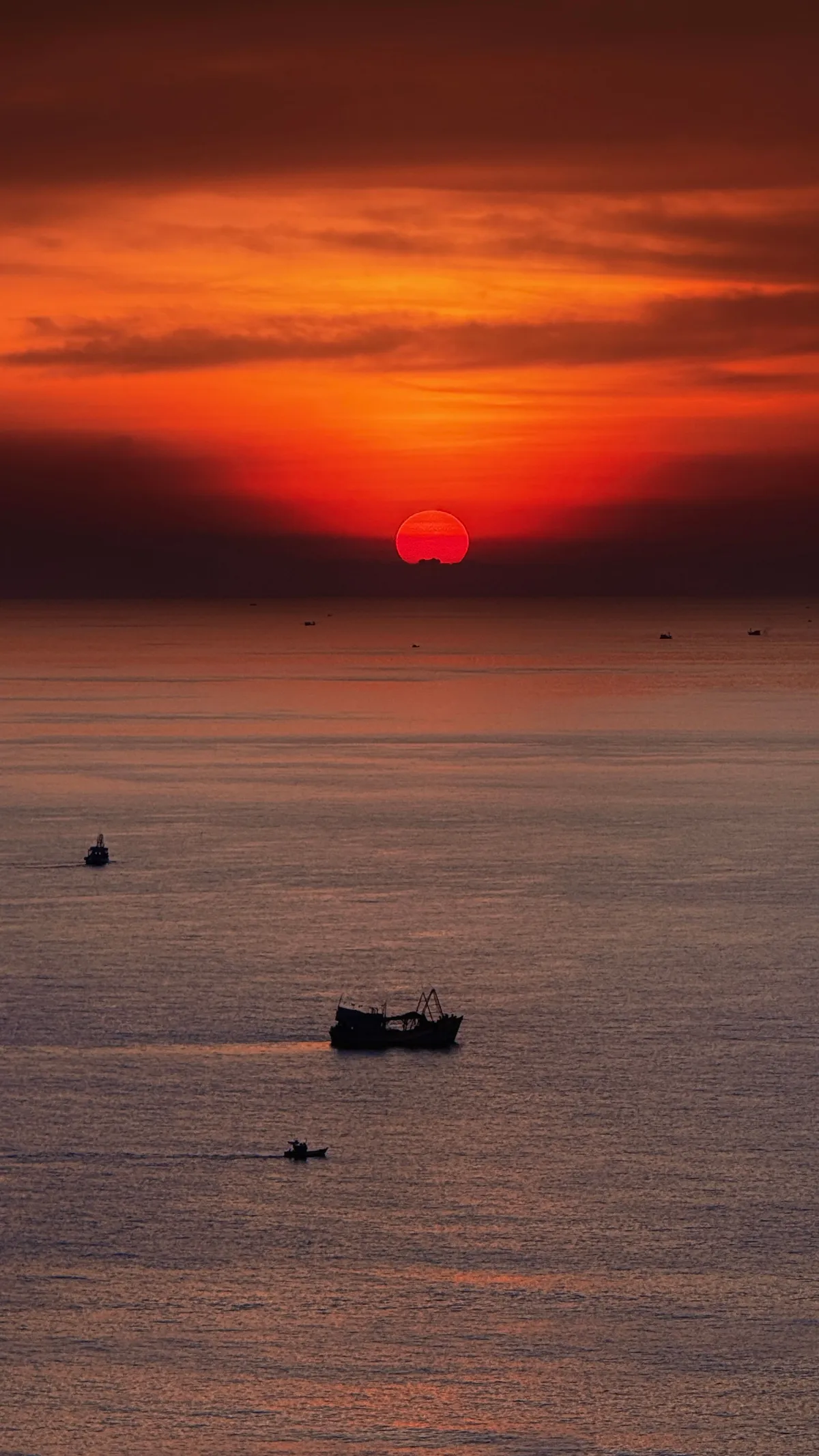 Deep orange sunset over the sea with a red sun on the horizon and two small fishing boats