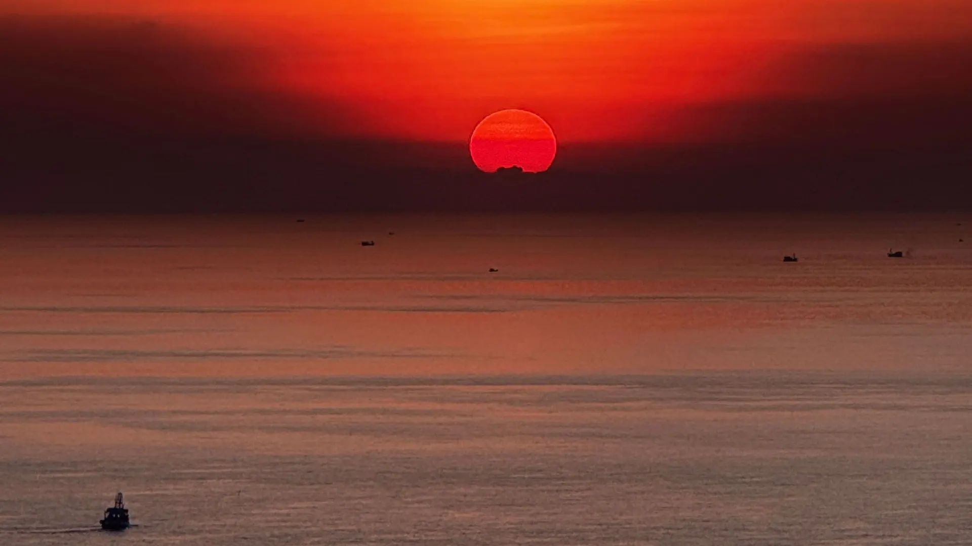 Deep orange sunset over the sea with a red sun on the horizon and two small fishing boats